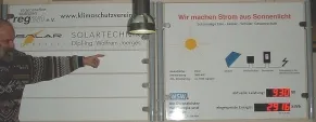 Im Foyer der Schule zeigt ein Mann auf die Anzeigetafel mit den aktuellen Werten der Solaranlage
