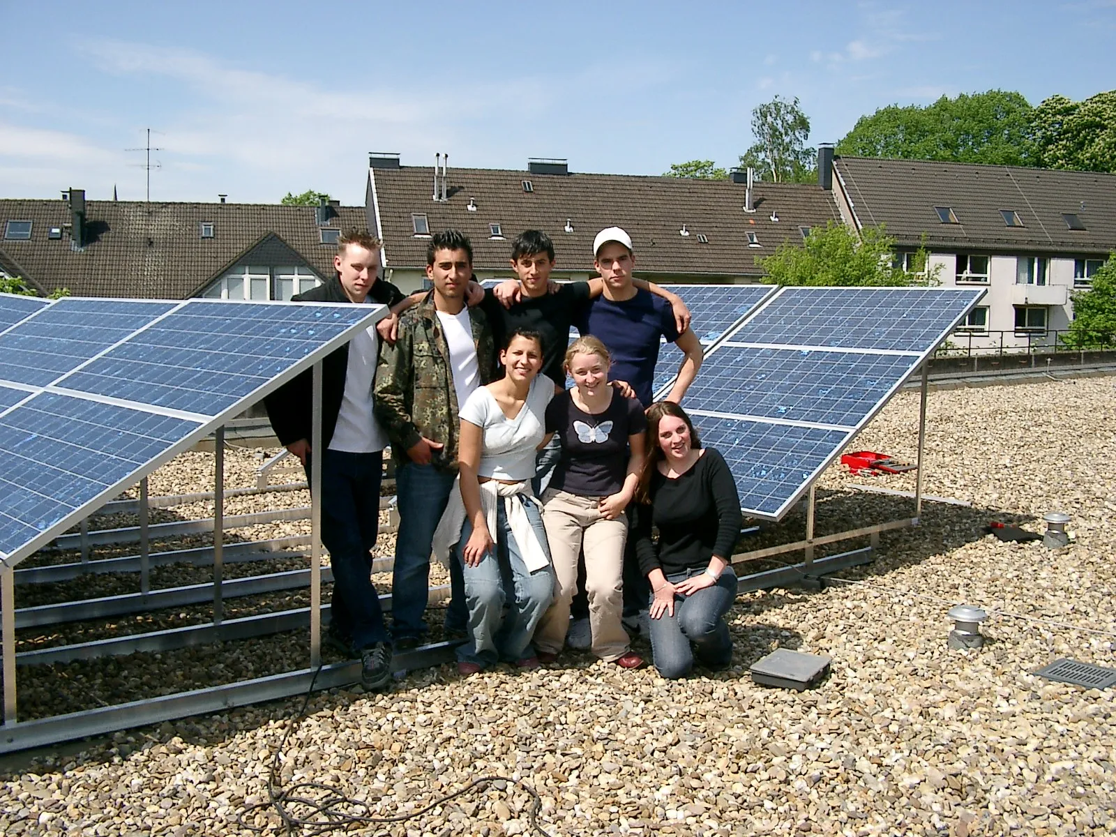 Acht Schülerinnen und Schüler stehen auf dem Schuldach zwischen zwei Reihen aufgeständerter Solarmodule