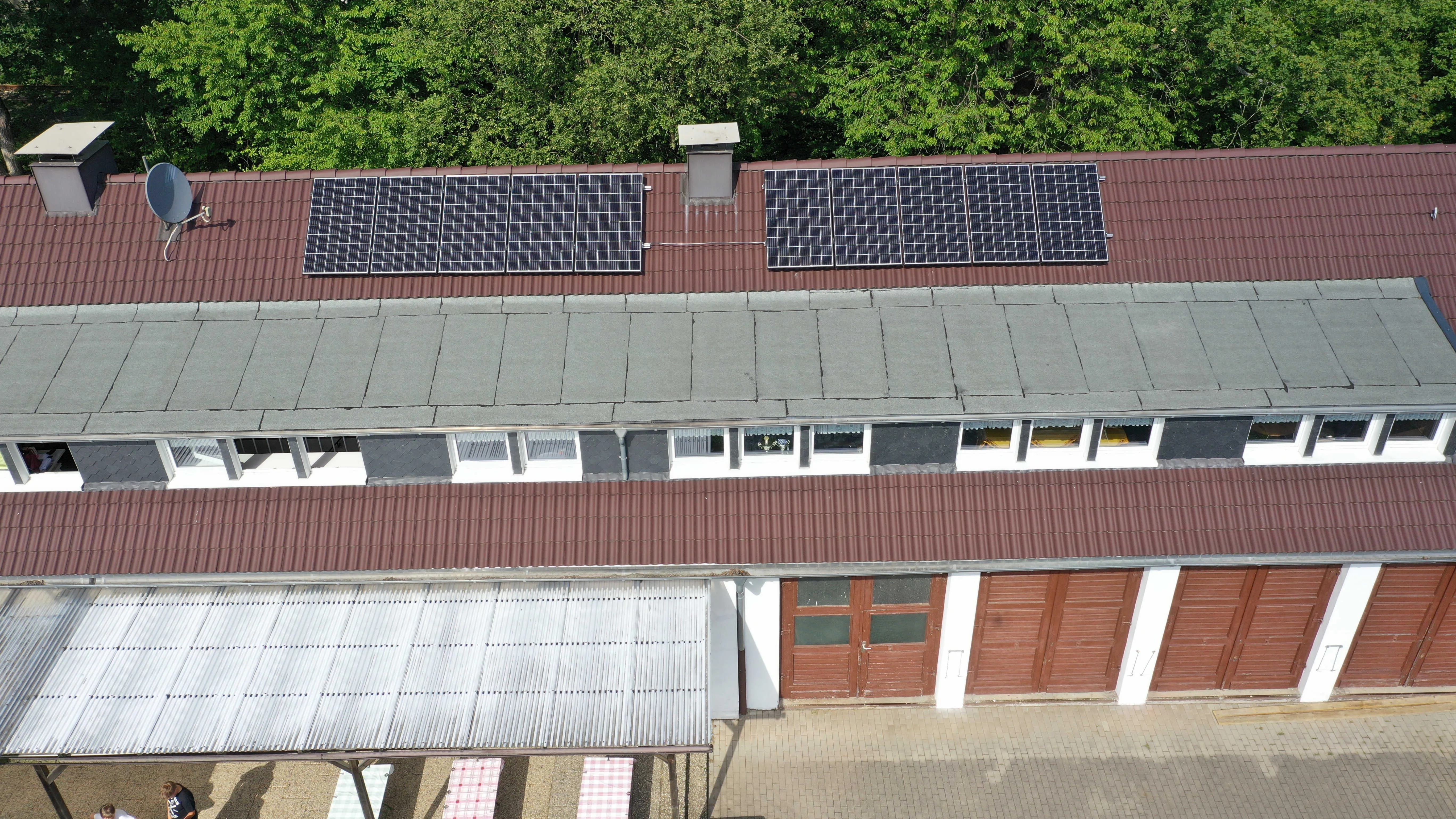 Luftbild des Bootshauses am Beyenburger Stausee: zwei Reihen Solarmodule auf dem roten Wellblechdach, dahinter Laubbäume