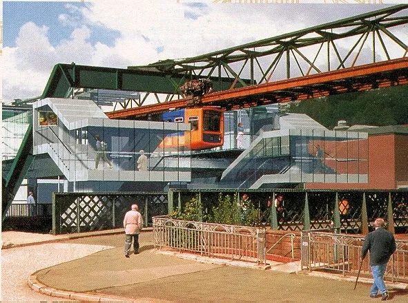 Schwebebahnhof Adlerbrücke mit verglastem Bahnsteigdach, darunter fährt ein orangefarbener Schwebebahnwagen ein